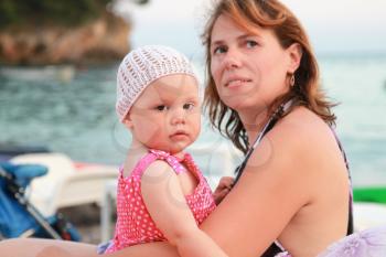 Brown-eyed young Caucasian mother with her baby girl sitting on the sea coast