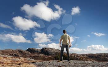 Young man staring at blue sky stands on rocky ground