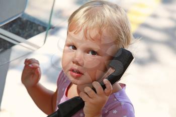Outdoor portrait of little blond girl talking on the street phone