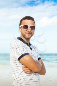 Outdoor portrait of young sporty Caucasian man standing with white sunglasses on summer sea coast