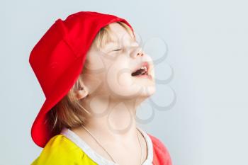 Studio portrait of happy baby girl in red baseball cap over gray wall background