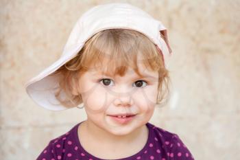 Outdoor closeup portrait of smiling cute Caucasian blond baby girl in white baseball cap