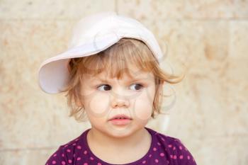 Outdoor closeup portrait of curious cute Caucasian blond baby girl in baseball cap