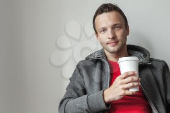 Portrait of young Caucasian man in gray hoodie with paper cup of Coffee