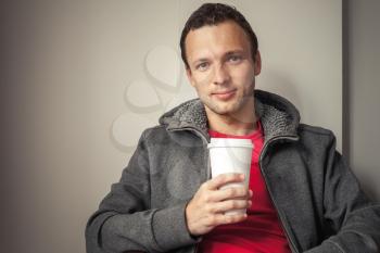 Portrait of young Caucasian man in hoodie sitting in cafe with paper cup of Coffee