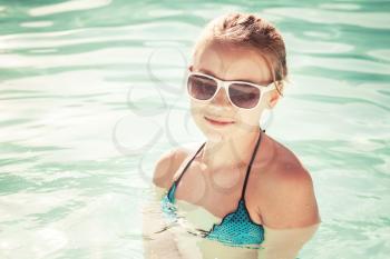 Beautiful little blond girl with sunglasses in outdoor pool, closeup summer portrait, vintage toned photo, old style filter effect