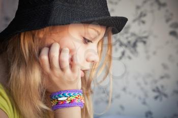 Profile portrait of beautiful blond teenage girl in black hat and rubber loom bracelets, toned photo, instagram style effect