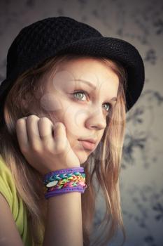 Portrait of beautiful blond teenage girl in black hat and rubber loom bracelets, vintage toned photo, instagram style effect