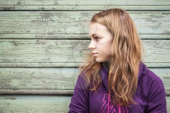 Beautiful blond Caucasian girl  teenager, closeup profile outdoor portrait over green wooden wall