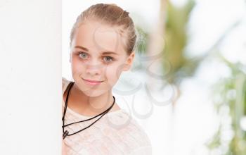 Outdoor portrait of beautiful blond Caucasian teenage girl near white wall in a park