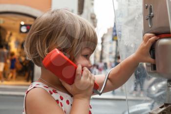 Outdoor portrait of little blond girl talking on the urban street phone