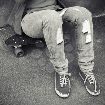 Teenager in jeans and gumshoes sits on a skateboard