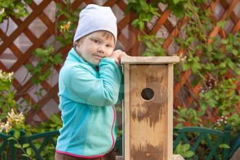 Cute smiling Caucasian blond girl stands near new handmade nesting box