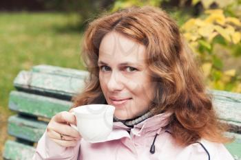 Young adult Caucasian woman drinks coffee in autumnal park