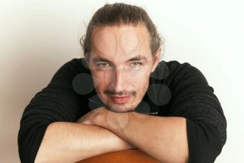 Positive young Asian man sitting on wooden chair, close-up studio portrait