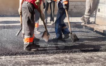 Urban road is under construction, asphalting in progress, group of workers in uniform with shovels