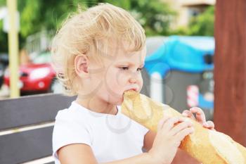 Outdoor closeup portrait of cute Caucasian blond baby girl eating French baguette