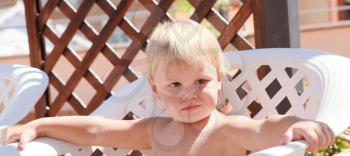 Small baby girl sitting in plastic armchair in a sunlight. Closeup outdoor portrait 