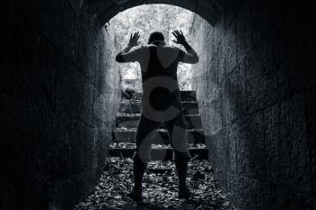 Man leaves dark stone tunnel with raised hands, surrender concept black and white photo 