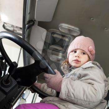 Cute Caucasian baby girl driving big cargo truck, square photo