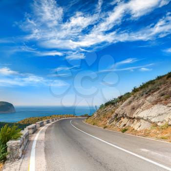 Turn of mountain highway with dramatic blue sky and sea on a background