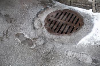 Sewer manhole on the urban asphalt road with wet snow