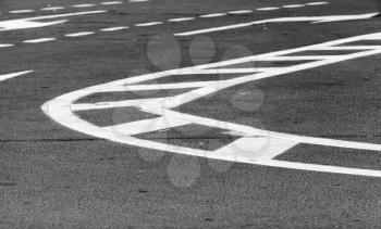 Abstract transportation background. White bent lines over dark gray asphalt, road marking. Selective focus with shallow DOF