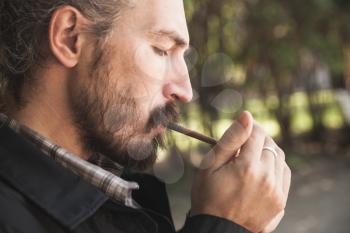 Bearded Asian man lights a cigarette, outdoor profile portrait with selective focus