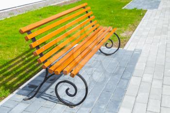 Empty wooden bench stands on cobblestone in summer park near green lawn grass