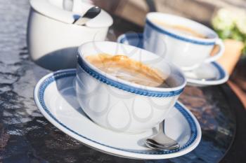 Two cups of cappuccino stand on glass table in street cafe, closeup photo with selective focus