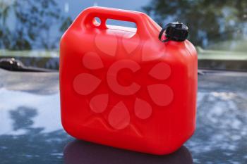 Red plastic jerry can stands on a car hood