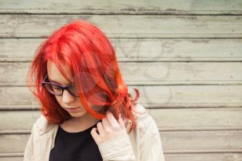 Caucasian teenager girl in glasses with bright red hair, closeup outdoor portrait over green grungy wooden wall