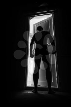Strong man stands near door in black room and looks inside opening to the light