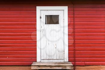 Small white closed door in red rural wooden wall, background photo texture. Scandinavian style