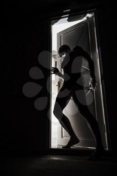 Man stands near door in black room and looks inside opening to the light