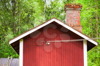 Facade fragment of traditional Scandinavian red wooden house over green forest background. Kotka, Finland