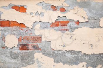 Old brick wall with damaged stucco and yellow paint layers, background photo texture