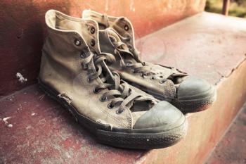 Pair of old sneakers standing on red concrete stairs, closeup photo with selective focus