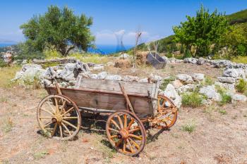 Empty old rural wooden wagon stands on summer field under clouded sky. Zakynthos, Greece