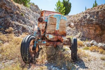 Old abandoned rusted tractor stands on dry summer grass, front view