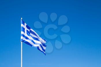 Flag of Greece waving on a flagpole over clear blue sky background