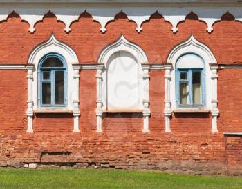 Red brick wall with windows in white decorative frames. Traditional ancient Russian architecture details