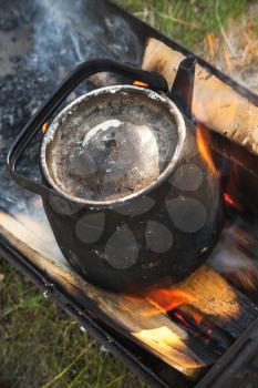 Old black boiling teapot on bonfire, vertical photo