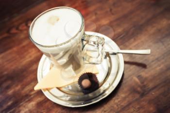 Glass mug full of Cappuccino stands on wooden table in cafeteria. Closeup photo with soft selective focus