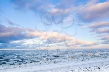 Winter coastal landscape with ice fragments and colorful cloudy sky. Gulf of Finland, Russia