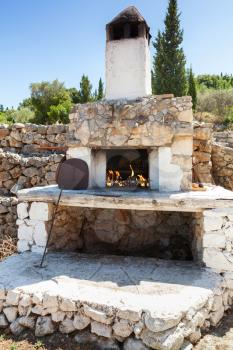 White outdoor stone oven with burning fire in summer garden. Greece