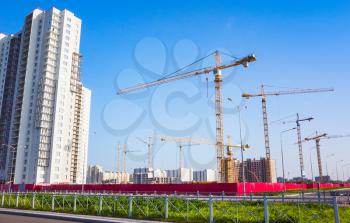 Block of flats under construction with cranes are under blue sky in summer day