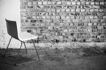 Abstract empty interior background, white office chair stands on concrete floor near brick wall, black and white photo