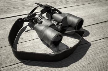 Black binoculars lays on rough outdoor wooden table, close-up photo with selective focus