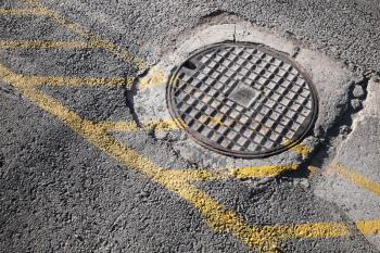 Round hatch in urban pavement, sewer manhole cover with yellow road marking lines